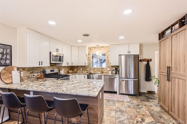 kitchen featuring a breakfast bar area, backsplash, appliances with stainless steel finishes, light stone counters, and a peninsula