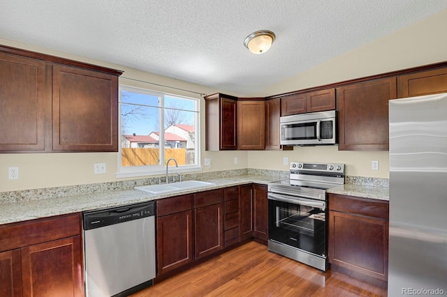 243 Madison Dr, Bennett, CO 80102 - kitchen with light stone counters, a sink, a textured ceiling, light wood-type flooring, and appliances with stainless steel finishes