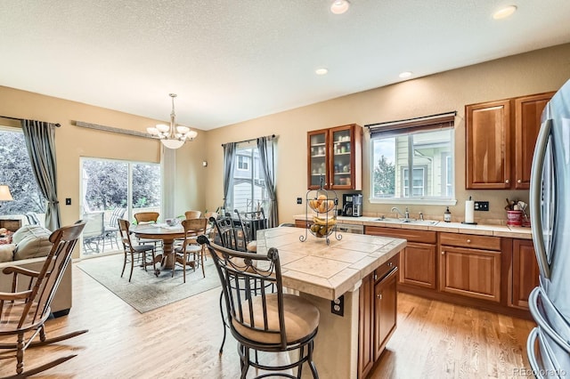 10463 Nucla St, Commerce City, CO 80022 - kitchen featuring tile counters, brown cabinetry, light wood-type flooring, a chandelier, and glass insert cabinets