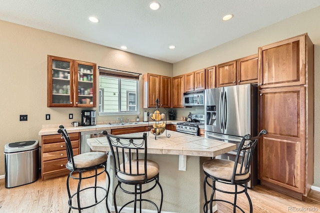 10463 Nucla St, Commerce City, CO 80022 - kitchen with stainless steel appliances, a breakfast bar, light wood-type flooring, a kitchen island, and glass insert cabinets