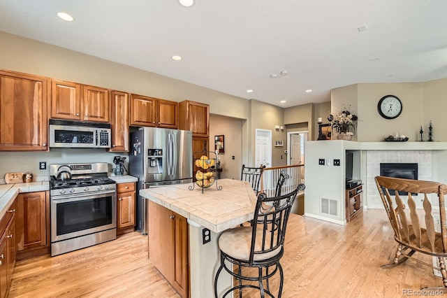 10463 Nucla St, Commerce City, CO 80022 - kitchen featuring stainless steel appliances, tile countertops, light wood-type flooring, brown cabinets, and a kitchen island