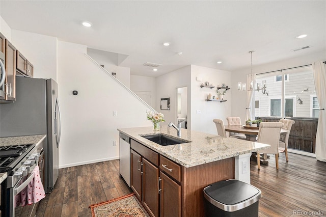 kitchen with sink, decorative light fixtures, appliances with stainless steel finishes, dark hardwood / wood-style flooring, and a kitchen island with sink