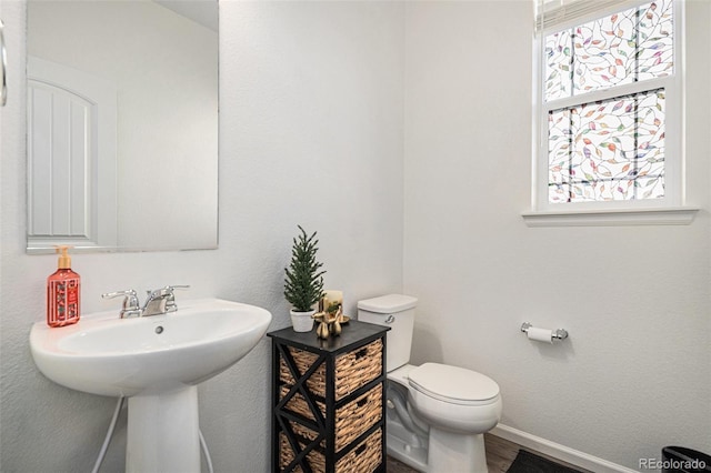 half bathroom with toilet, wood finished floors, and baseboards