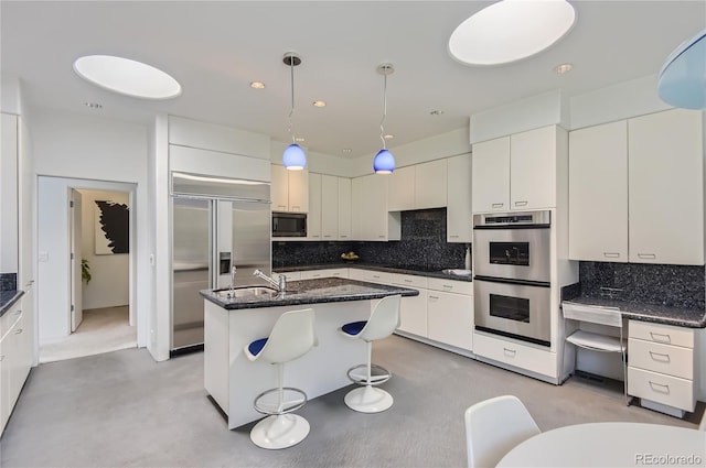 kitchen featuring pendant lighting, an island with sink, white cabinets, decorative backsplash, and stainless steel appliances