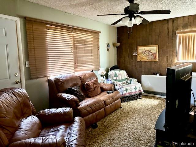 living room with ceiling fan, a textured ceiling, and wood walls