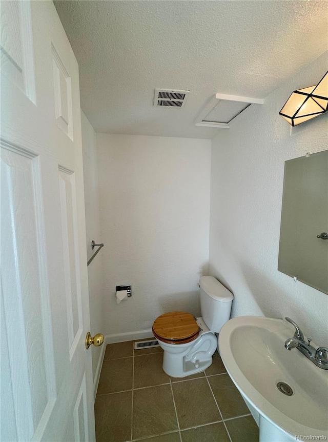 bathroom with a textured ceiling, toilet, sink, and tile patterned floors