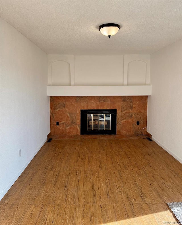 unfurnished living room with a stone fireplace, wood-type flooring, and a textured ceiling