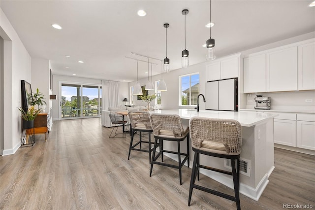 kitchen with white cabinets, light countertops, a kitchen island with sink, freestanding refrigerator, and open floor plan