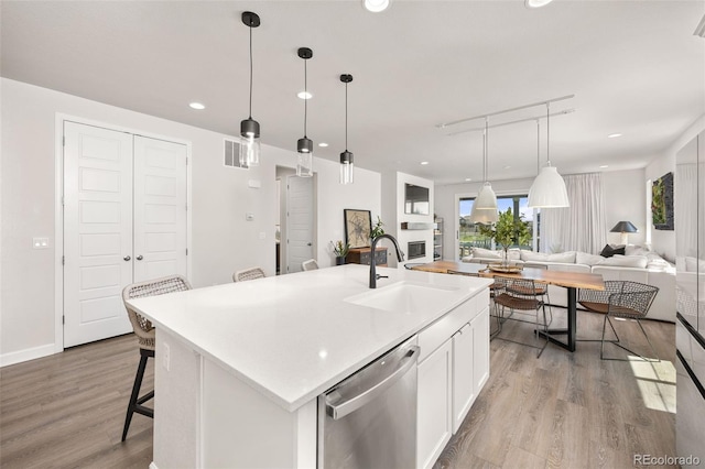 kitchen featuring white cabinets, a sink, light wood finished floors, dishwasher, and open floor plan