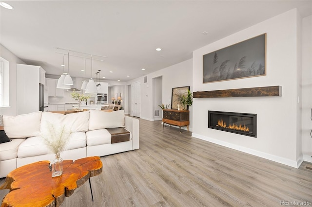 living area with visible vents, baseboards, light wood finished floors, a glass covered fireplace, and recessed lighting
