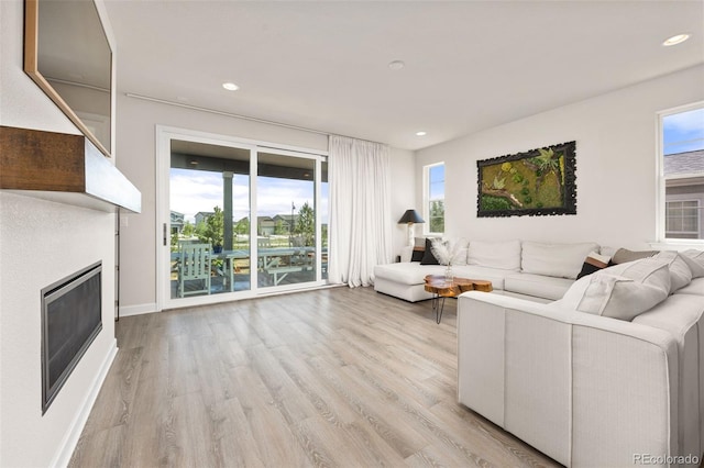 living room featuring light wood-type flooring, recessed lighting, plenty of natural light, and a glass covered fireplace