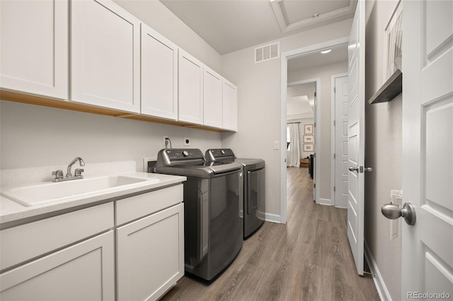 washroom with independent washer and dryer, visible vents, wood finished floors, cabinet space, and a sink