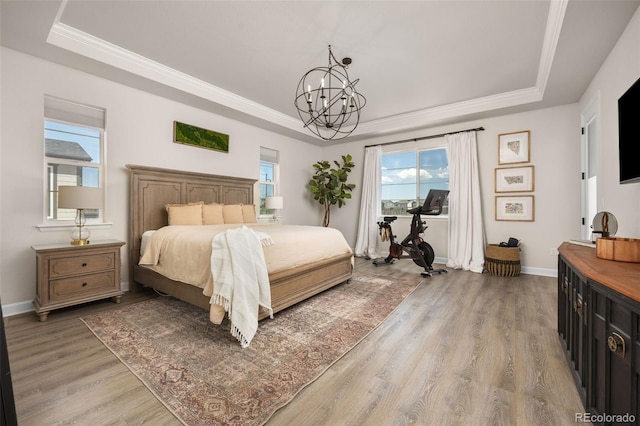 bedroom featuring light wood-style floors, multiple windows, a tray ceiling, and a chandelier