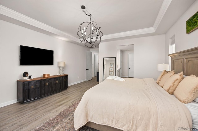 bedroom featuring an inviting chandelier, a raised ceiling, baseboards, wood finished floors, and ornamental molding