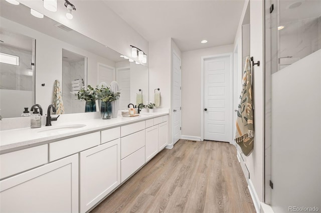bathroom featuring double vanity, a sink, walk in shower, and wood finished floors
