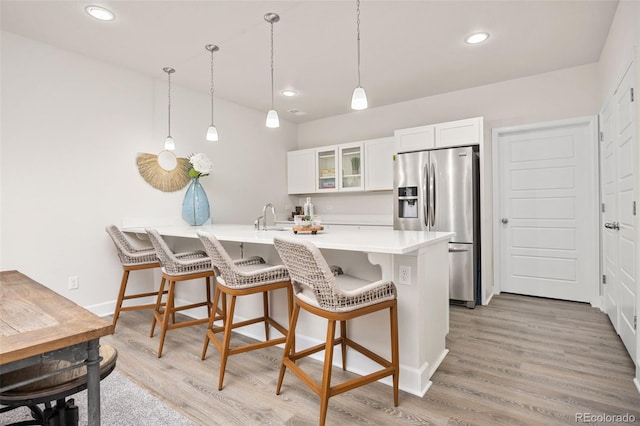 kitchen with a breakfast bar area, white cabinetry, a peninsula, stainless steel refrigerator with ice dispenser, and glass insert cabinets