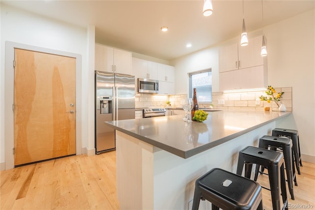 6892 Juniper Ct, Arvada, CO 80007 - kitchen featuring stainless steel appliances, a peninsula, a breakfast bar, light wood-type flooring, and recessed lighting