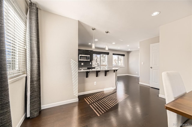 kitchen featuring light stone counters, dark hardwood / wood-style floors, pendant lighting, decorative backsplash, and a breakfast bar area