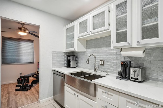 kitchen with white cabinets, sink, stainless steel dishwasher, decorative backsplash, and light stone countertops