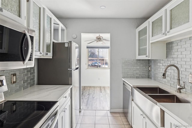 kitchen featuring light tile patterned floors, baseboards, a ceiling fan, appliances with stainless steel finishes, and white cabinetry