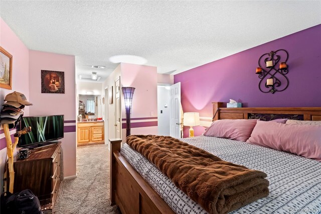 bedroom featuring ensuite bath, a textured ceiling, and light colored carpet