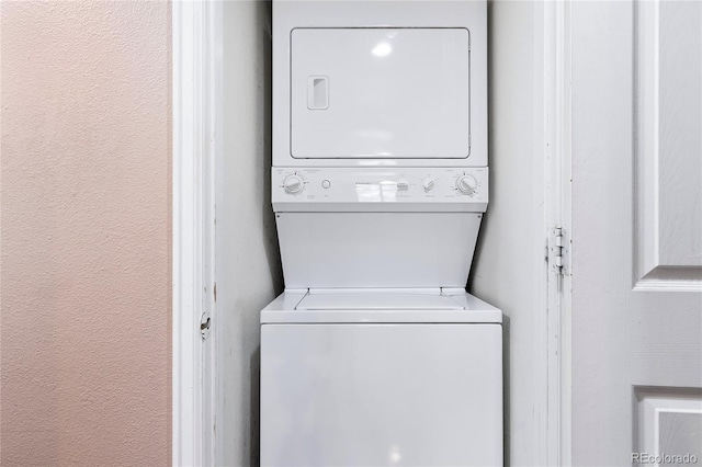 clothes washing area featuring a textured wall, laundry area, and stacked washing maching and dryer