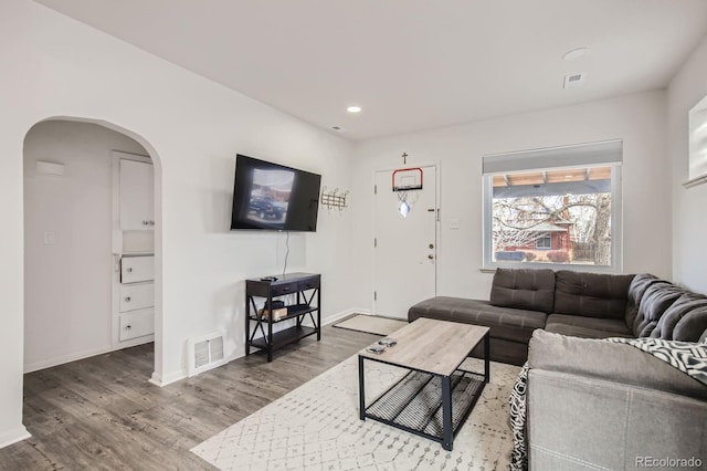 living room featuring visible vents, arched walkways, baseboards, and wood finished floors