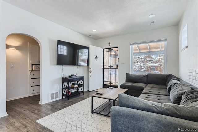 living room featuring arched walkways, visible vents, baseboards, and wood finished floors