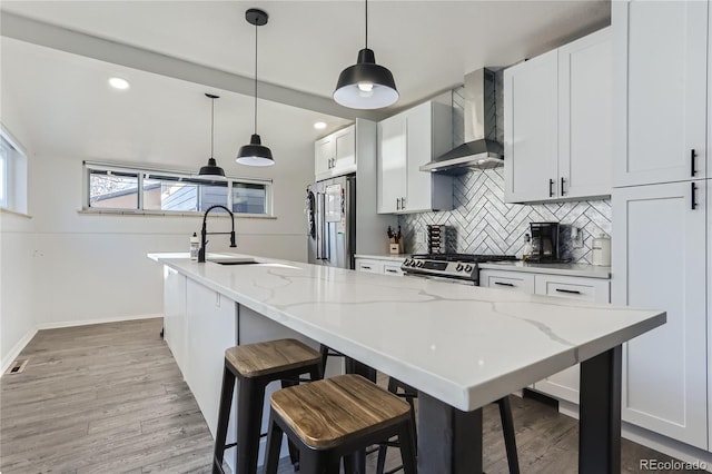 kitchen featuring a sink, stainless steel appliances, a kitchen bar, wall chimney exhaust hood, and backsplash