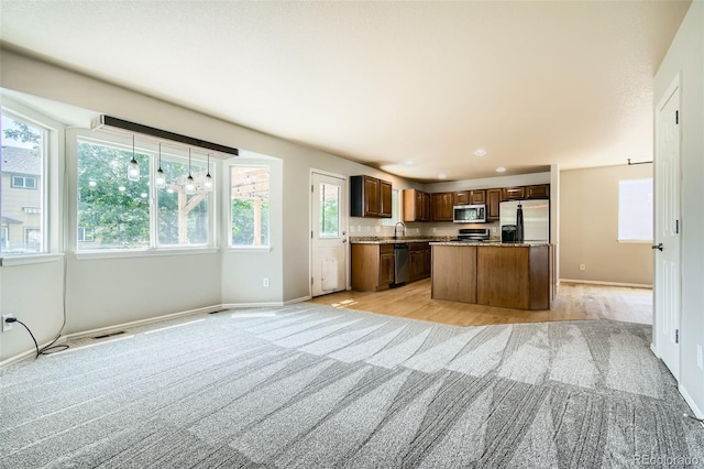 13018 Niagara Way, Thornton, CO 80602 - kitchen with stainless steel appliances, open floor plan, a kitchen island, light carpet, and dark brown cabinets