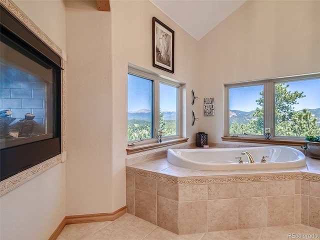 bathroom with tile patterned flooring, vaulted ceiling, a mountain view, and tiled tub