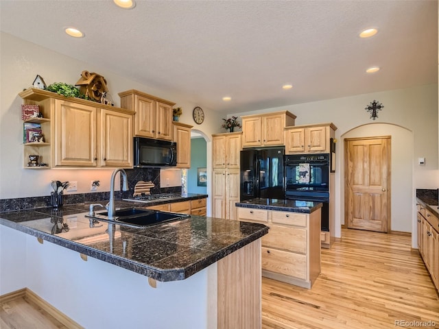 kitchen featuring a breakfast bar, black appliances, sink, light hardwood / wood-style floors, and kitchen peninsula