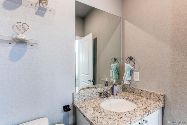 bathroom with a textured wall, vanity, and toilet