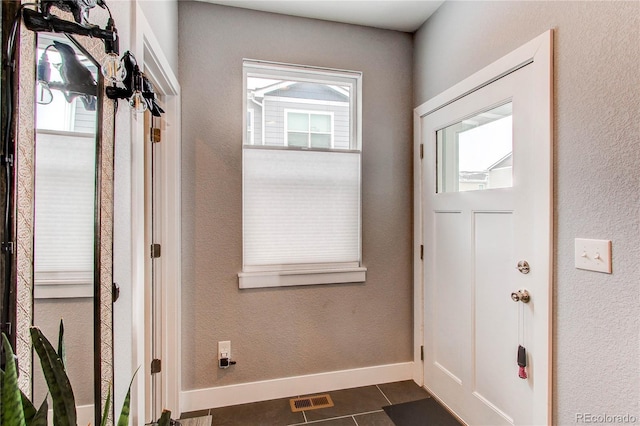 doorway with dark tile patterned floors, visible vents, baseboards, and a textured wall