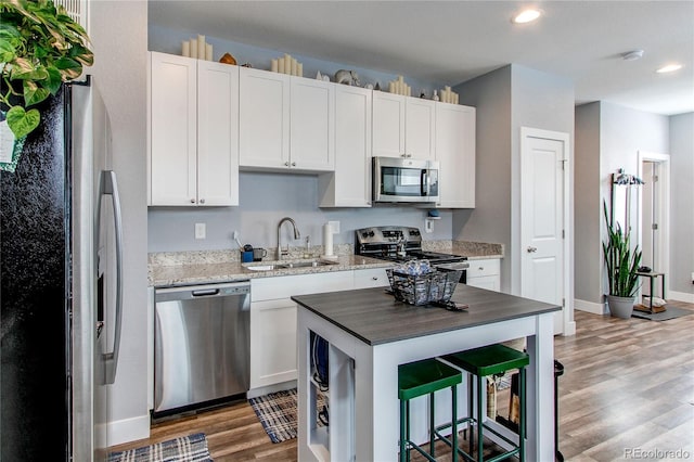 kitchen featuring white cabinets, appliances with stainless steel finishes, a breakfast bar, light wood-style floors, and a sink