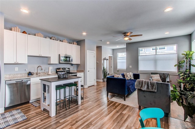 kitchen featuring appliances with stainless steel finishes, open floor plan, white cabinetry, a sink, and light wood-type flooring