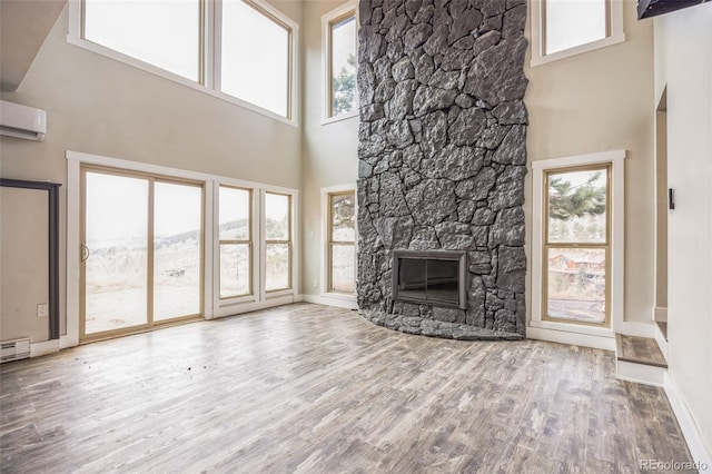 unfurnished living room with a fireplace, a wall unit AC, wood-type flooring, and a high ceiling