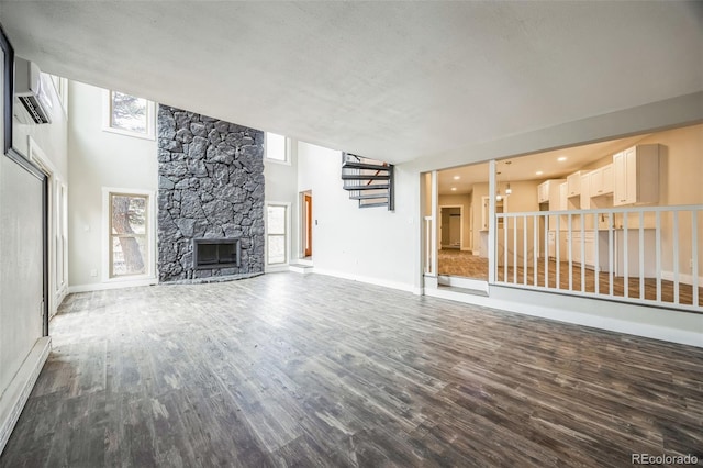 unfurnished living room featuring a wall unit AC, a high ceiling, a fireplace, wood-type flooring, and a textured ceiling