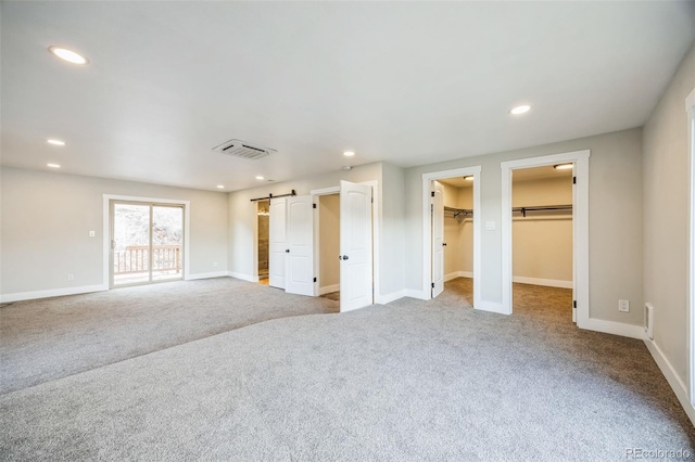 unfurnished bedroom featuring a barn door, light carpet, and a spacious closet