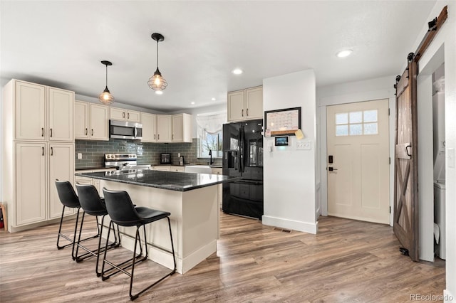 741 Cortez St, Denver, CO 80221 - kitchen featuring appliances with stainless steel finishes, a barn door, a breakfast bar, and light wood finished floors