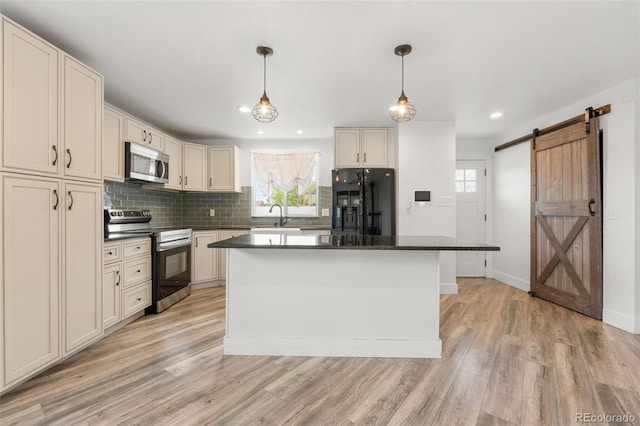 741 Cortez St, Denver, CO 80221 - kitchen featuring appliances with stainless steel finishes, dark countertops, a barn door, light wood-style flooring, and decorative backsplash