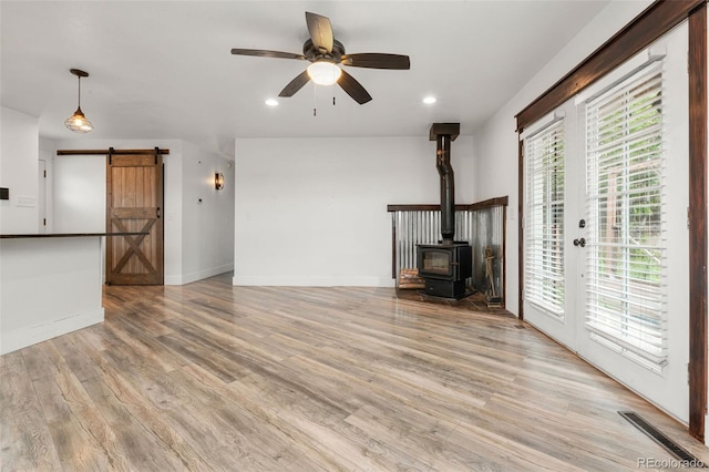 741 Cortez St, Denver, CO 80221 - unfurnished living room with a barn door, ceiling fan, a wood stove, light wood finished floors, and recessed lighting