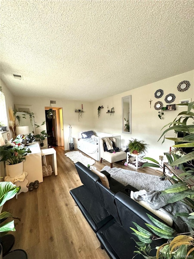 living room with a textured ceiling, visible vents, and wood finished floors