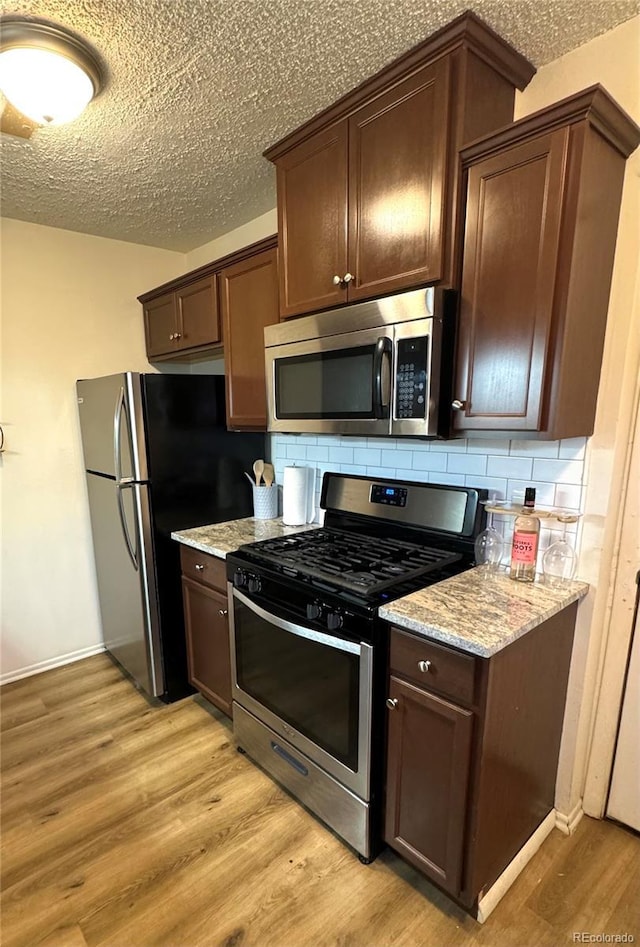 kitchen with a textured ceiling, stainless steel appliances, dark brown cabinets, light wood finished floors, and tasteful backsplash