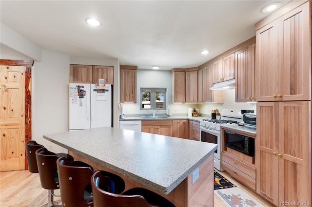 33002 Bobcat Ct, Trinidad, CO 81082 - kitchen featuring white appliances, under cabinet range hood, a kitchen bar, light brown cabinetry, and light countertops