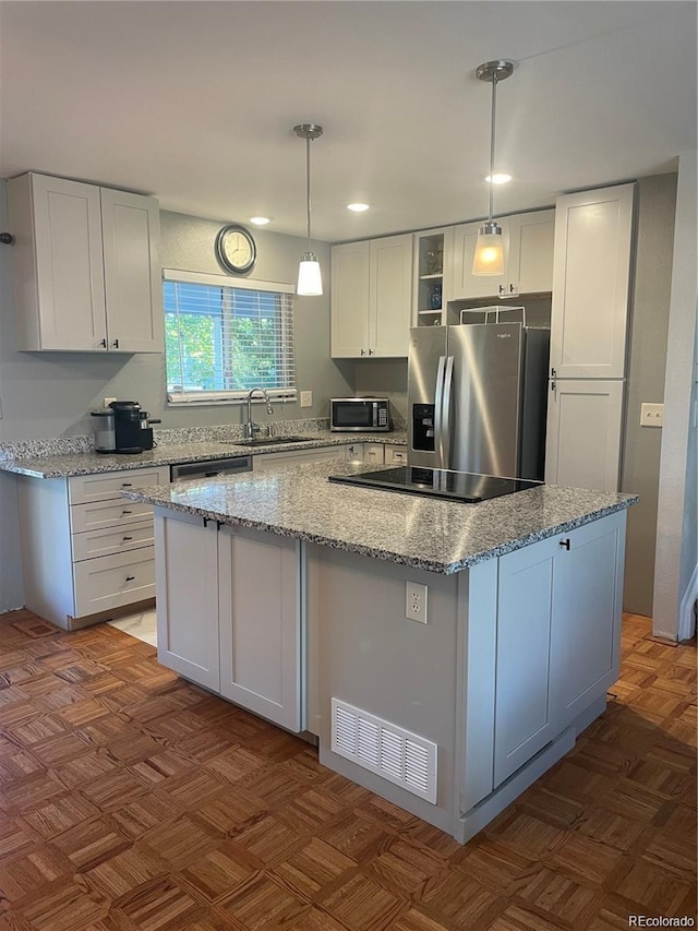 kitchen with visible vents, a sink, appliances with stainless steel finishes, white cabinetry, and a center island