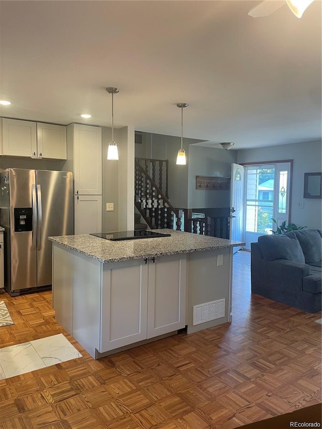 kitchen featuring light stone counters, visible vents, stainless steel fridge, black electric stovetop, and open floor plan