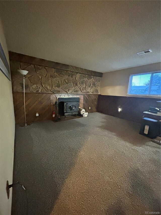 interior space with wooden walls, visible vents, carpet flooring, a wood stove, and a textured ceiling