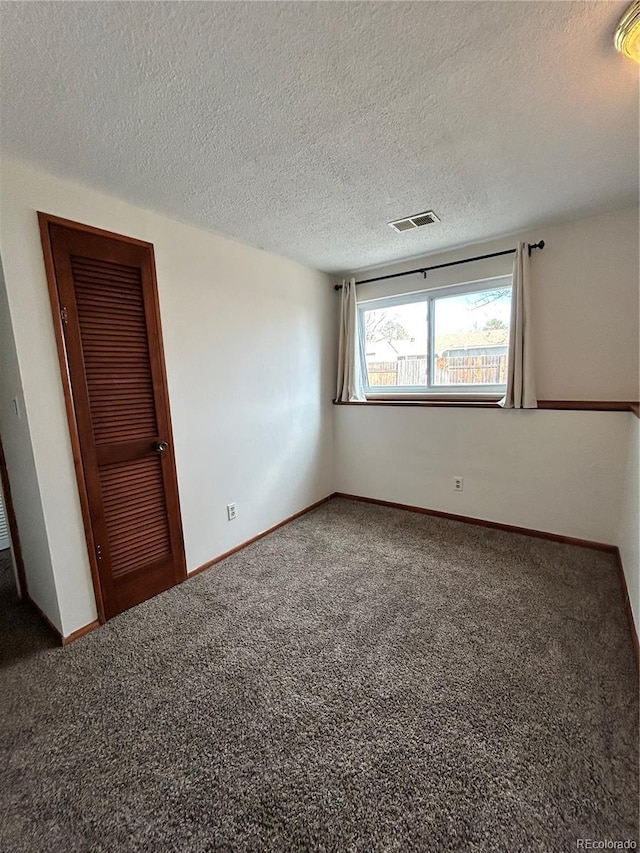 carpeted spare room with visible vents, a textured ceiling, and baseboards