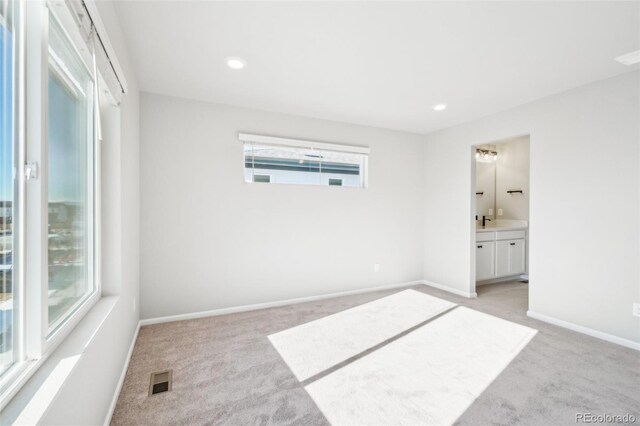 unfurnished bedroom with ensuite bathroom, light colored carpet, and multiple windows